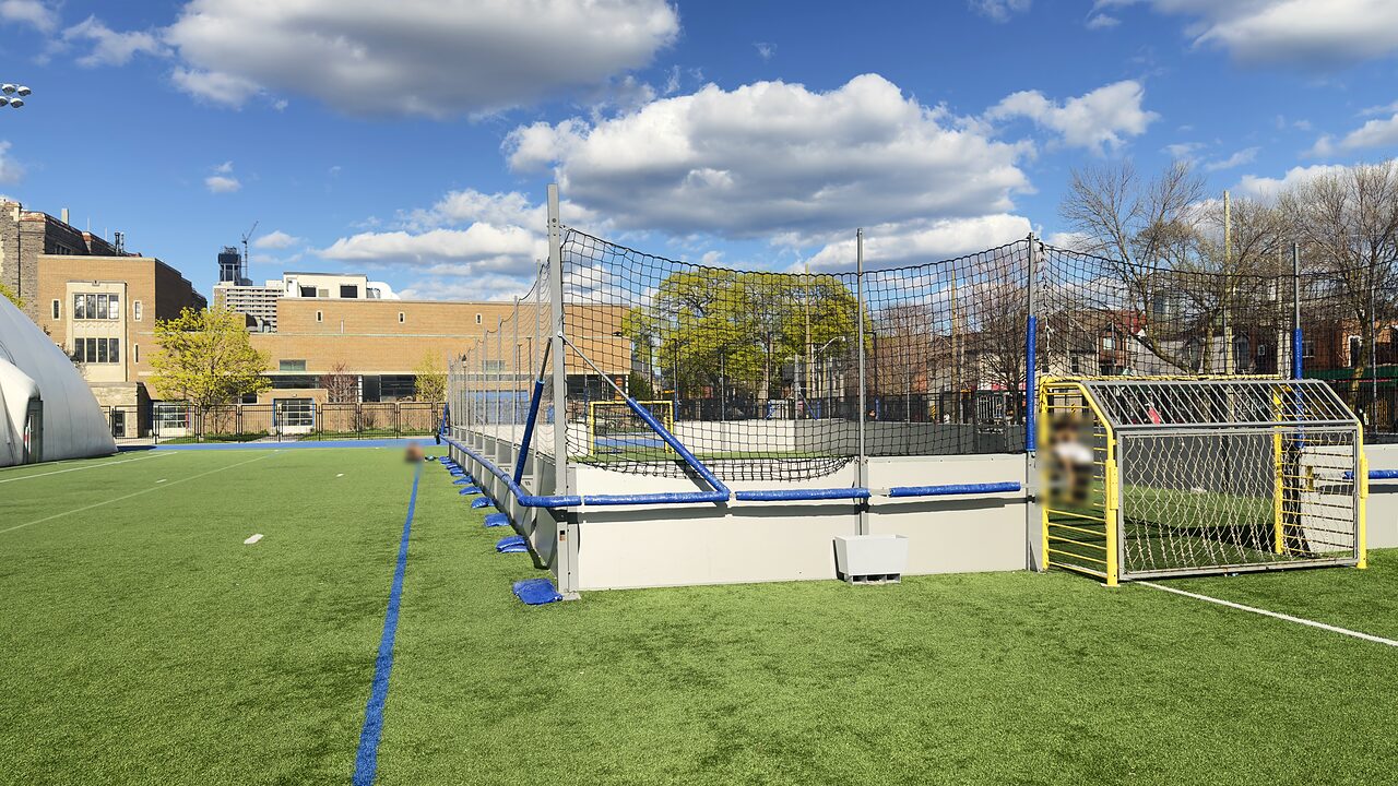 Wide view of KICKR's 5v5 caged turf court at Central Tech Stadium in Toronto, with the Toronto skyline and Central Tech's air-supported dome behind it