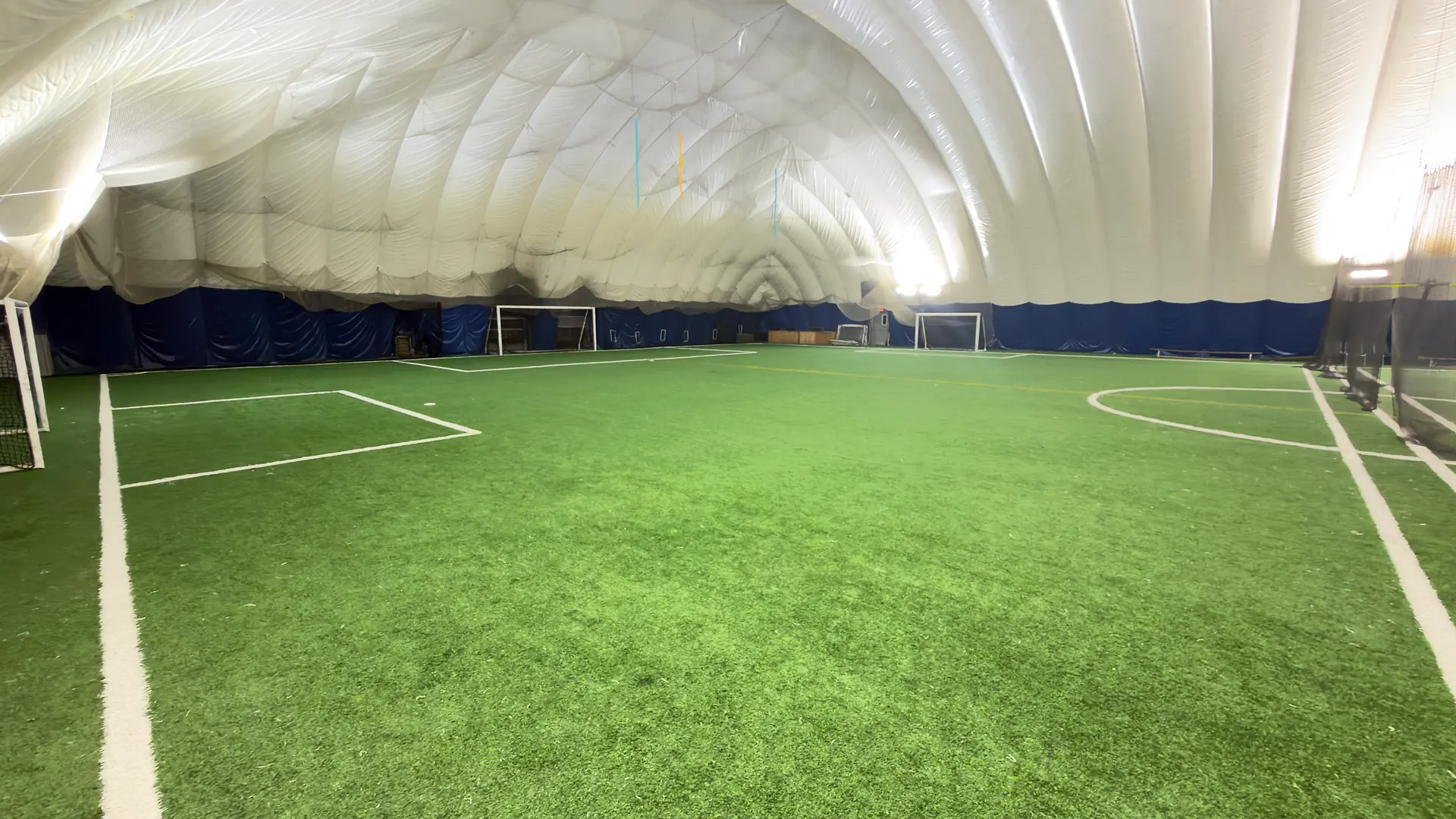 Wide view of the indoor turf field and goals under the white air dome